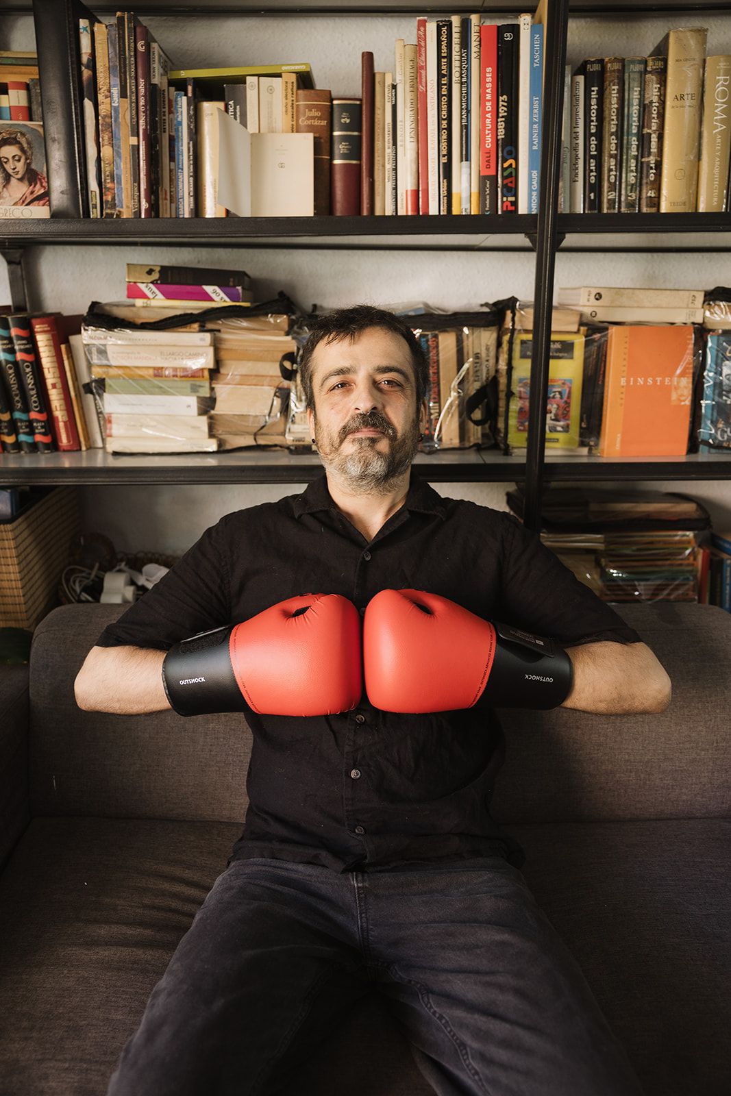 Toni Cervantes con guantes de boxeo, sentado frente a una estantería de libros